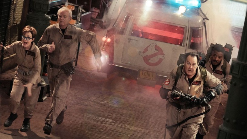 The original Ghostbusters running while Ecto-1 is in the background