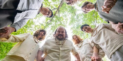 Characters stood holding hands, looking down at the camera, in Let's Start a Cult.