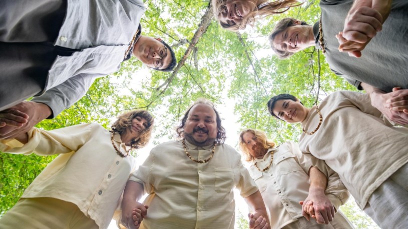 Characters stood holding hands, looking down at the camera, in Let's Start a Cult.