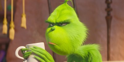 The Grinch holding a mug, looking grumpy.