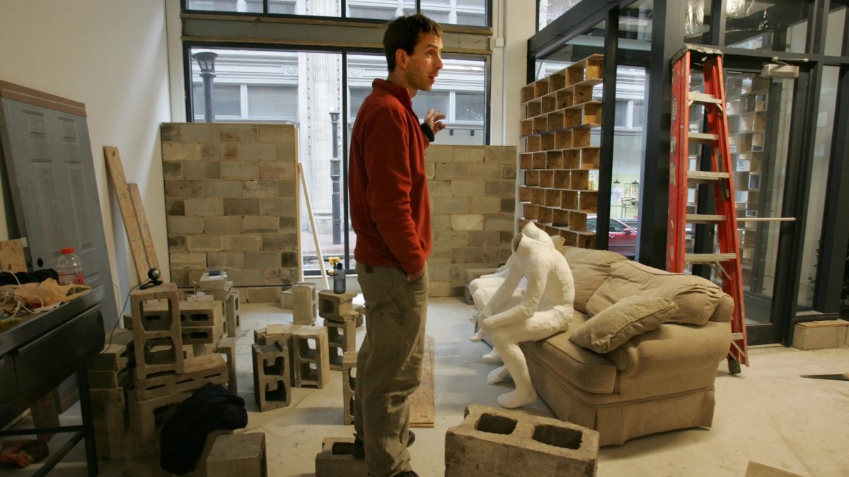 A person stood around a sofa and loose bricks in Secret Mall Apartment.